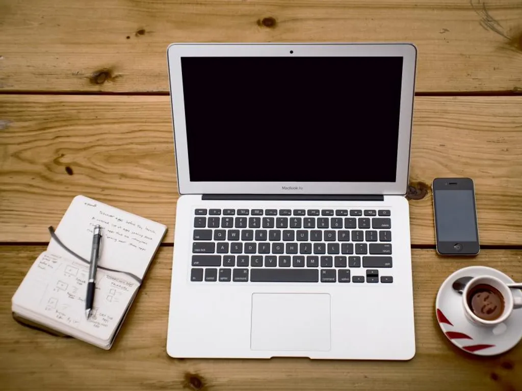 A laptop, notebook and coffee on a wooden desk