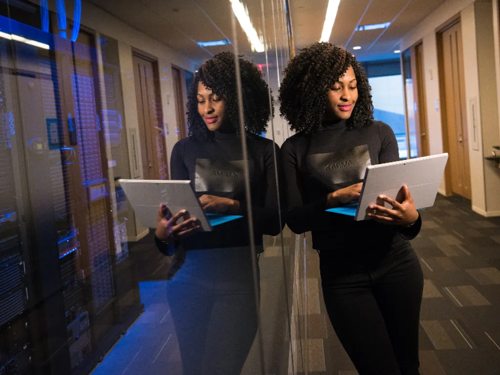 An engineer with a tablet in a server room, reflected in the glass