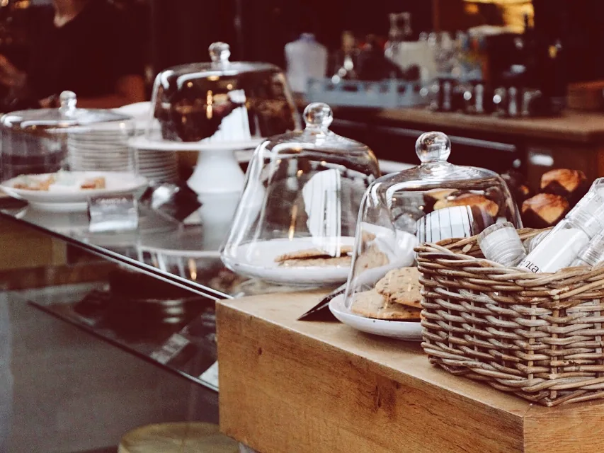 A café counter with cakes under glass domes and a basket of biscuits